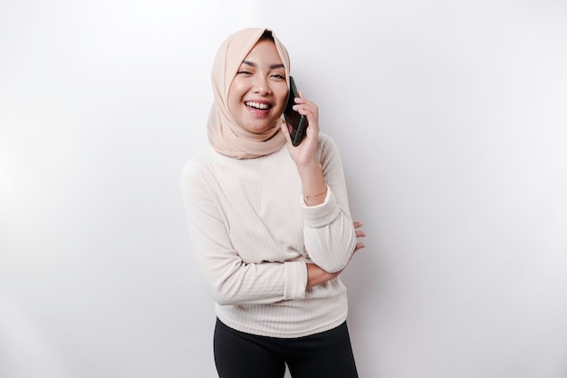 Uma mulher muçulmana asiática feliz usando um lenço na cabeça segurando seu telefone isolado por fundo branco