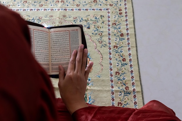 Uma mulher muçulmana sentada em um tapete de oração e lendo o Alcorão com tradução indonésia