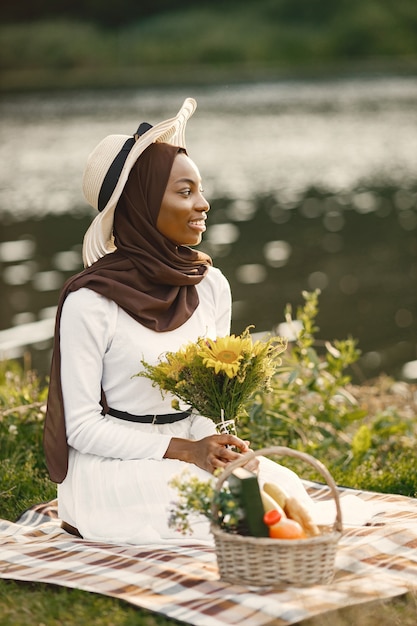 Uma mulher muçulmana sentada na manta de piquenique xadrez perto do rio