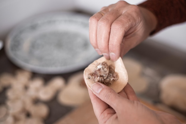 Uma mulher na cozinha esculpe bolinhos de massa com recheio de carne cozinhando deliciosos caseiros