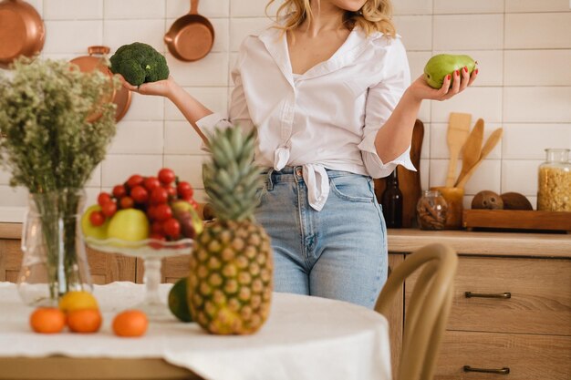 Uma mulher na cozinha segura legumes e frutas em suas mãos Legumes e frutas estão sobre a mesa em foco suave cozinhando