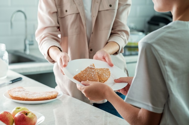 Uma mulher na cozinha serve um prato de torta de maçã para o filho