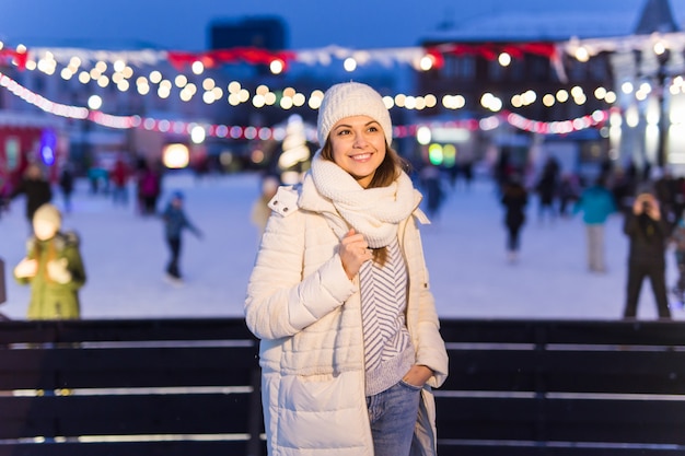 Uma mulher na pista está patinando e tomando selfie no smartphone. véspera de ano novo e natal. luzes de fadas. conceito de humor de gelo e neve. inverno