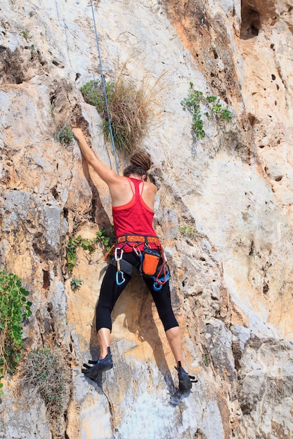 Uma mulher nova com uma corda acoplou nos esportes da escalada na rocha.