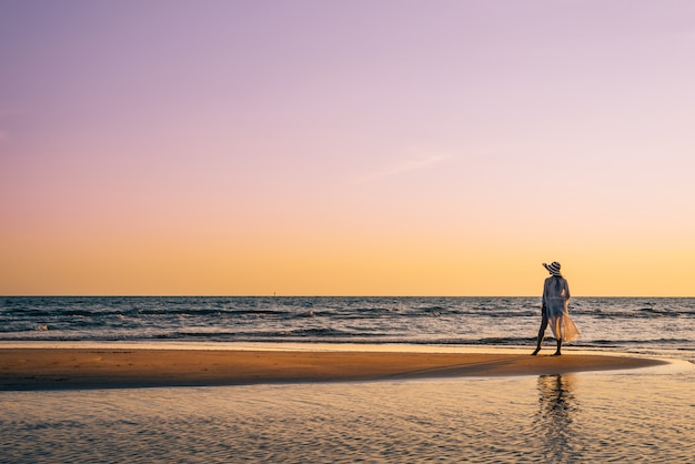 Uma mulher nova está na praia durante um por do sol, férias de verão.