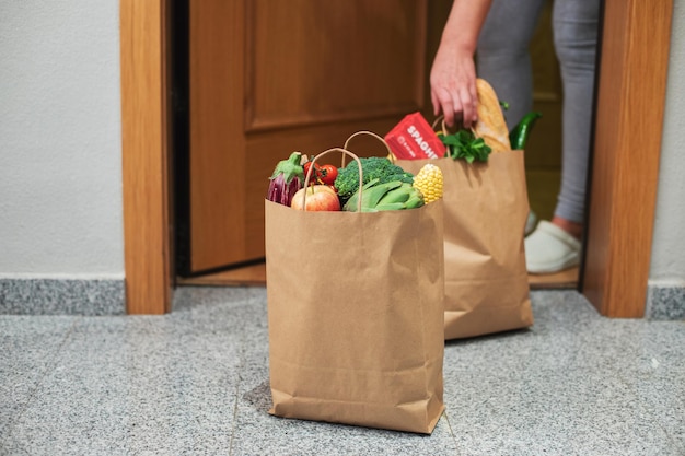 Uma mulher pega uma sacola de comida na porta de sua casa. Coronavírus. Quarentena. Ficar em casa, fazer compras online. Entrega de vegetais e frutas durante a quarentena e auto-isolamento