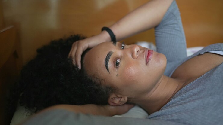 Foto uma mulher pensativa na cama brincando com o cabelo descansando