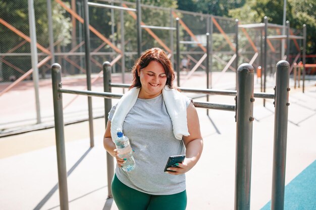 Uma mulher plus size após um treino ao ar livre encontra alegria com seu smartphone, seu sorriso irradia