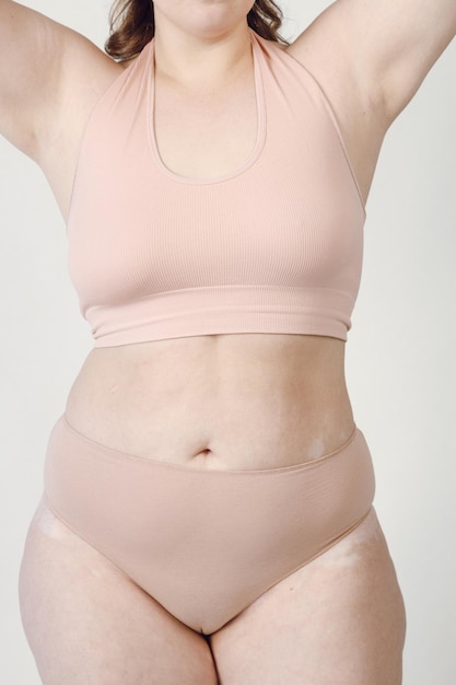 Uma mulher plussize acima do peso com estrias na pele em pé de cueca branca.