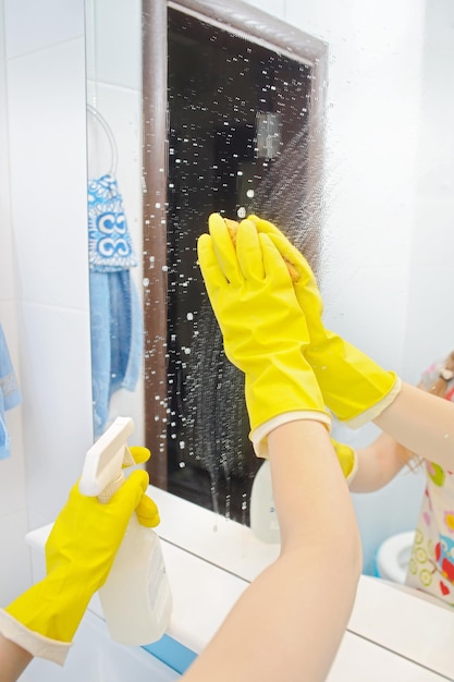 Uma mulher polindo vidro usando uma esponja de limpeza e luvas de borracha limpando um espelho