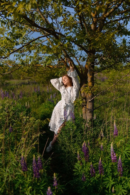 Uma mulher posando perto de uma árvore em um campo desfrutando dos raios do sol