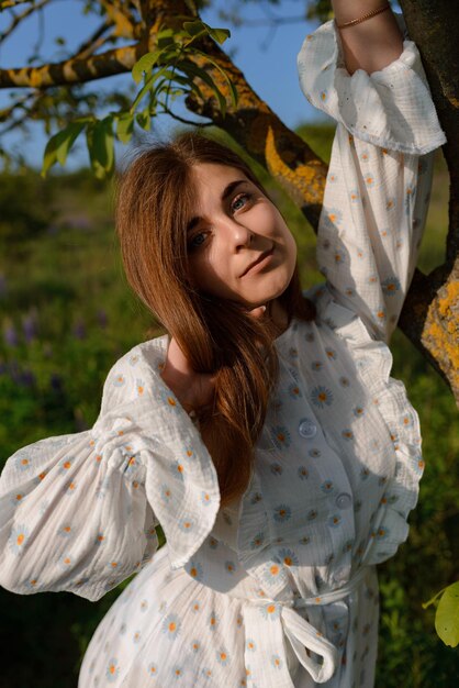 Uma mulher posando perto de uma árvore em um campo desfrutando dos raios do sol