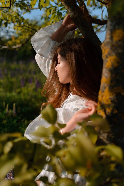 Foto uma mulher posando perto de uma árvore em um campo desfrutando dos raios do sol