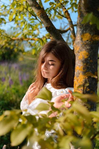 Uma mulher posando perto de uma árvore em um campo desfrutando dos raios do sol