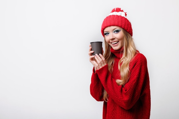 Uma mulher positiva em um suéter vermelho de inverno com um copo descartável em um fundo cinza