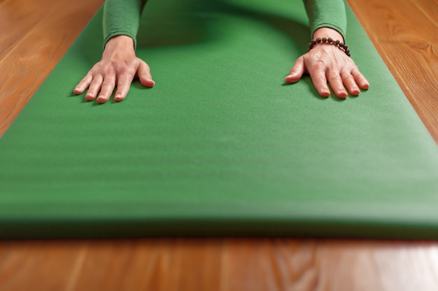 Uma mulher pratica ioga em um tapete verde em casa, na sala de estar. Asanas em Hatha yoga, fitness e esportes em casa.