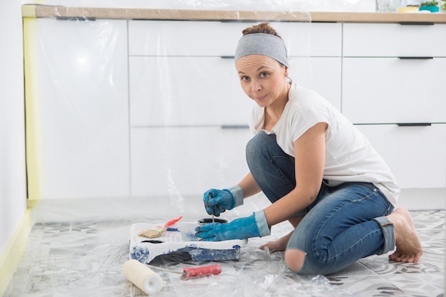 Uma mulher prepara tinta para pintar as paredes da cozinha Preparação de ferramentas e tintas para pintar