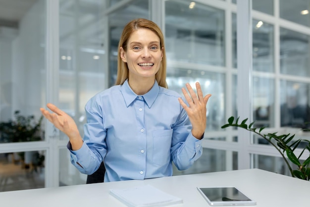 Foto uma mulher profissional com uma camisa azul faz gestos animados enquanto olha para uma câmera implicando um vídeo
