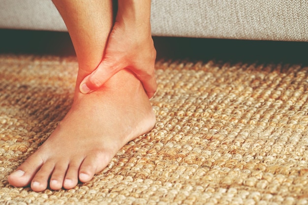 Uma mulher que sofre de dor no joelho sentada no sofá em casa massageando seu joelho doloroso Cuidados de saúde e conceito médico