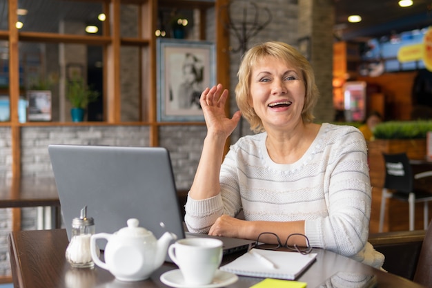 Uma mulher que trabalha com um laptop em uma mesa em um café. a mulher trabalha remotamente. ela ri