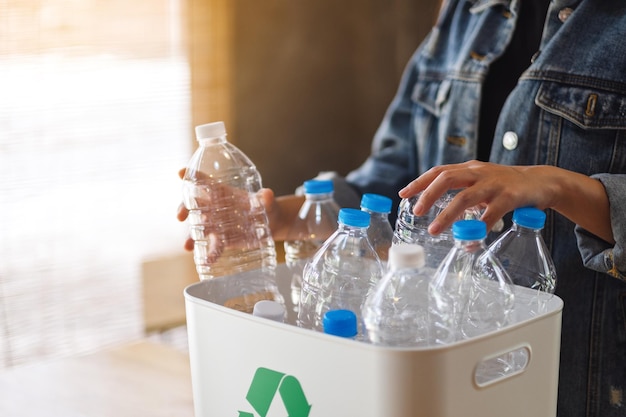 Uma mulher recolhendo e separando garrafas plásticas de lixo reciclável em uma lixeira em casa