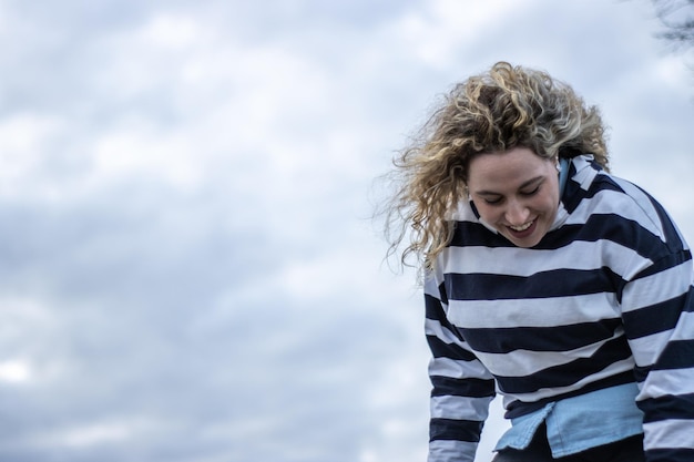 Uma mulher rindo alto ao ar livre contra um fundo de céu nublado