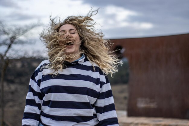 Uma mulher rindo com o cabelo ao vento ao ar livre em um dia nublado