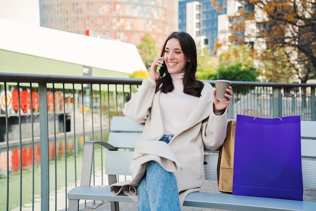 Uma mulher se senta em um banco e fala ao telefone enquanto segura uma bolsa roxa.