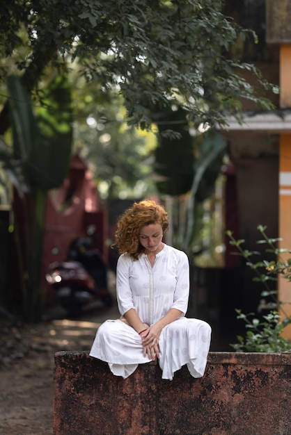 Uma mulher se senta em um banco na frente de uma casa