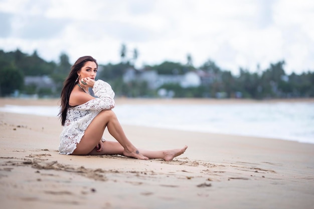 Uma mulher se senta na praia e olha para a câmera.