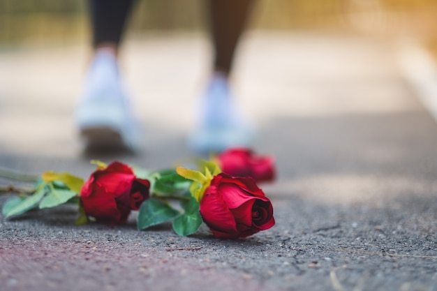 Uma mulher se vira e se afasta de uma flor de rosas vermelhas no chão