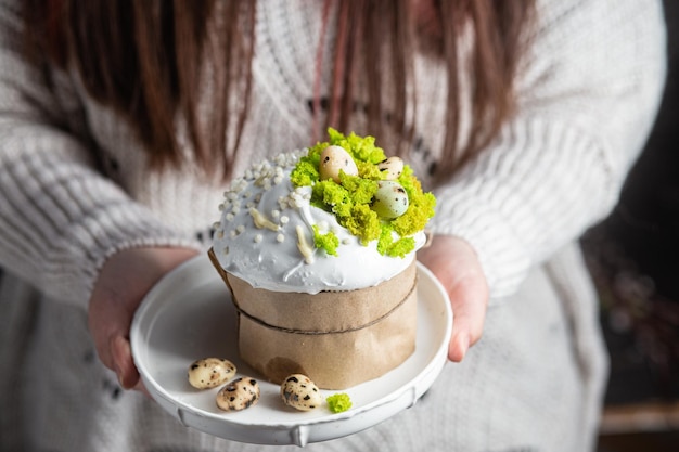 Uma mulher segura nas mãos um bolo de Páscoa com merengue e decoração em um prato