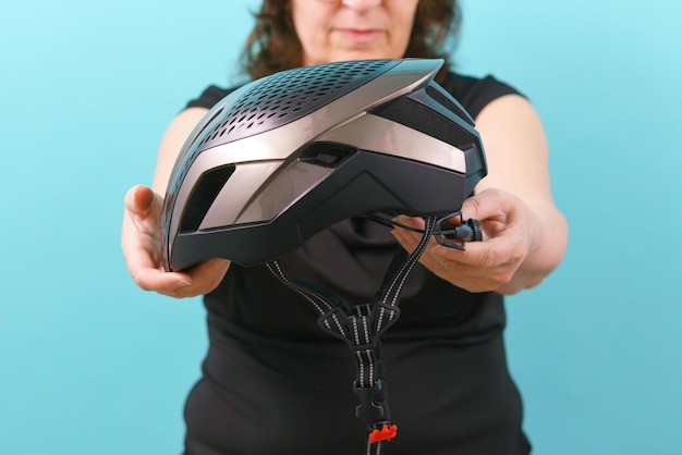 Uma mulher segura um capacete de bicicleta na frente de seu rosto em um fundo azul Equipamento Segurança Motociclista Estilo de vida adulto Confiança em pé Transporte Ciclismo Cabeça com aparência feminina