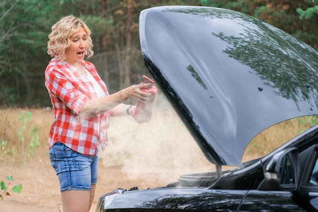 Foto uma mulher segura um extintor de incêndio em suas mãos enquanto está no capô aberto de um carro do qual vem fumaça