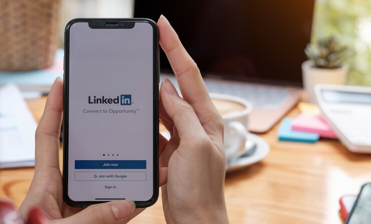 Uma mulher segura um smartphone com o aplicativo LinkedIn na tela. LinkedIn é um aplicativo de compartilhamento de fotos para smartphones.