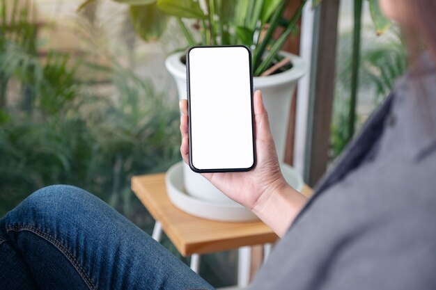 uma mulher segurando e usando telefone celular preto com tela em branco no café