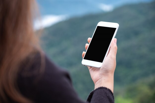 uma mulher segurando o telefone inteligente branco com tela em branco no exterior