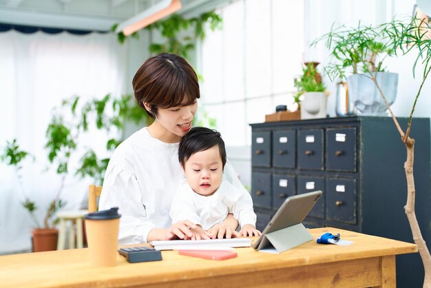Uma mulher segurando um bebê e operando um computador dentro de casa