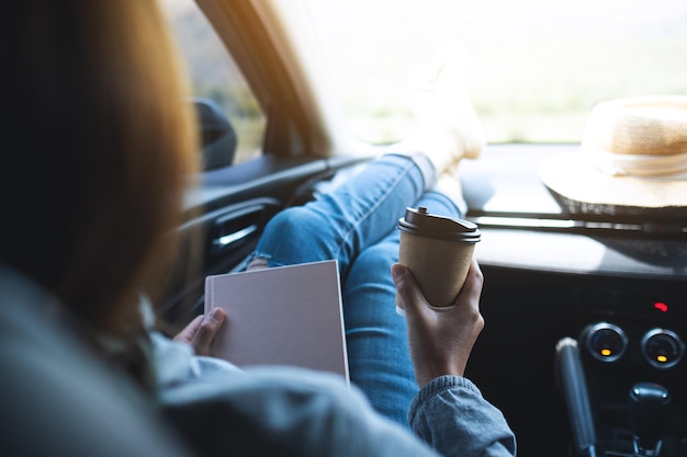 Uma mulher segurando um livro e tomando café no carro