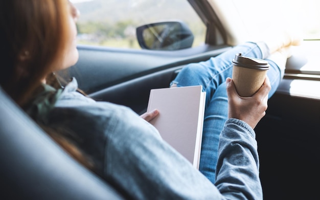 Uma mulher segurando um livro e tomando café no carro