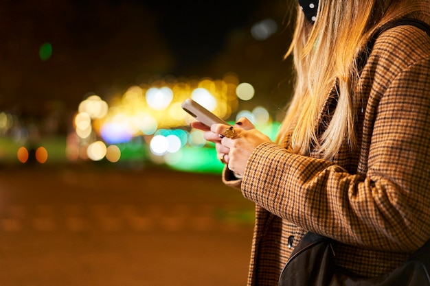 Uma mulher segurando um smartphone ao ar livre em uma cidade à noite.