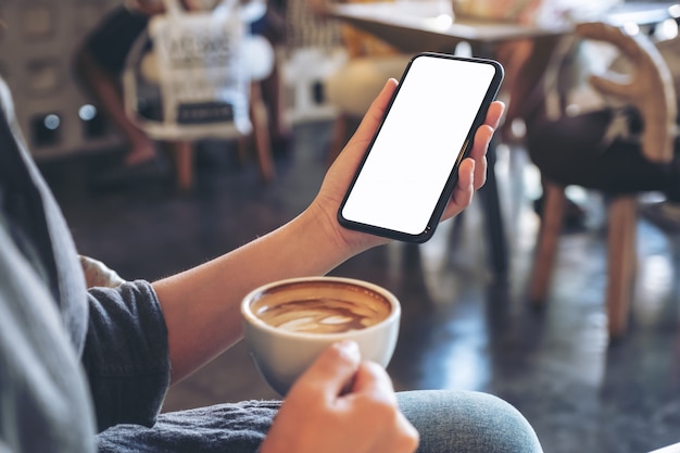 uma mulher segurando um telefone celular branco com uma tela em branco enquanto toma café em um café moderno