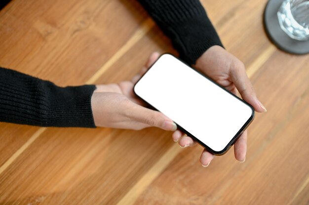 Uma mulher segurando uma maquete de tela branca de smartphone sobre uma mesa de madeira