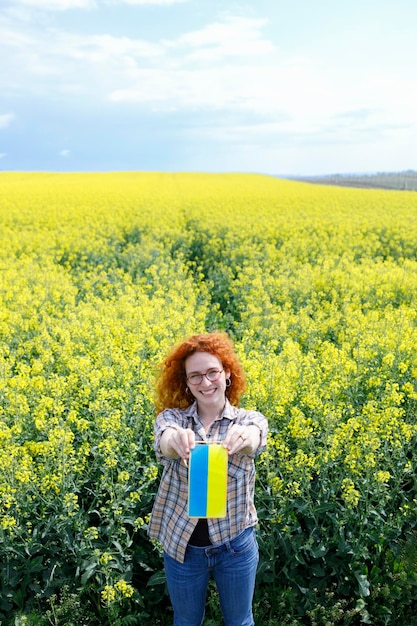 Uma mulher segurando uma pequena bandeira ucraniana em um campo de flores amarelas