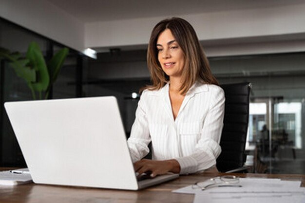 uma mulher senta-se em uma mesa com um laptop e um documento ao fundo