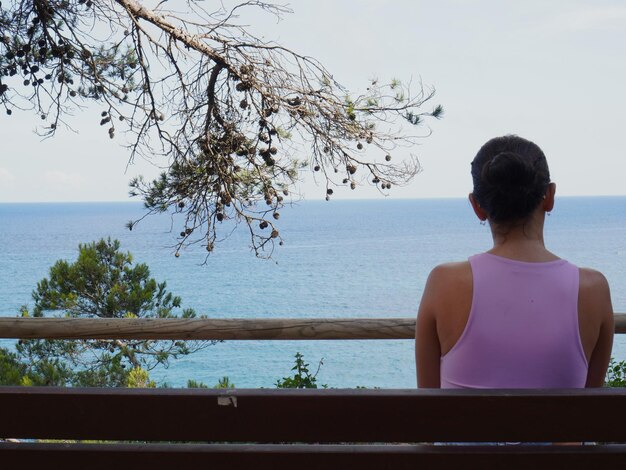 uma mulher senta-se num banco de madeira com vista para o oceano