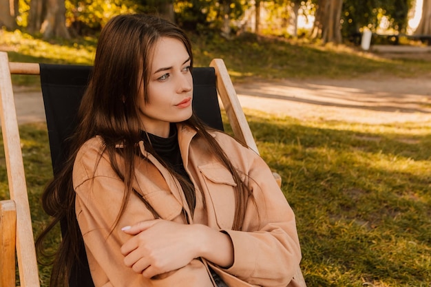 Uma mulher sentada em uma cadeira em um parque olhando para longe da câmera