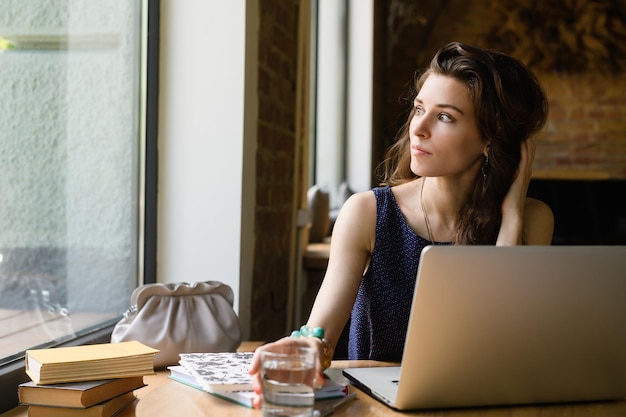 Uma mulher sentada em uma mesa com livros e um laptop em uma cafeteria