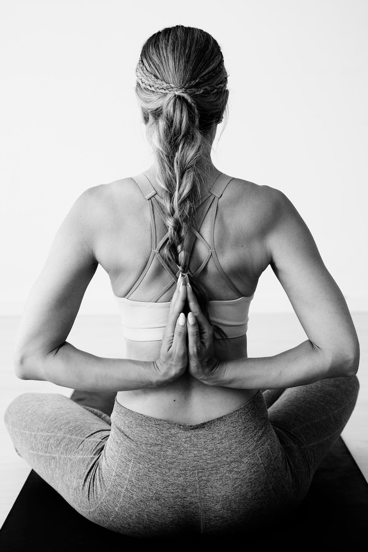 Foto uma mulher sentada na posição de lótus com as mãos em anjali mudra nas costas