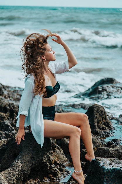 Uma mulher sentada nas rochas contra o fundo do mar